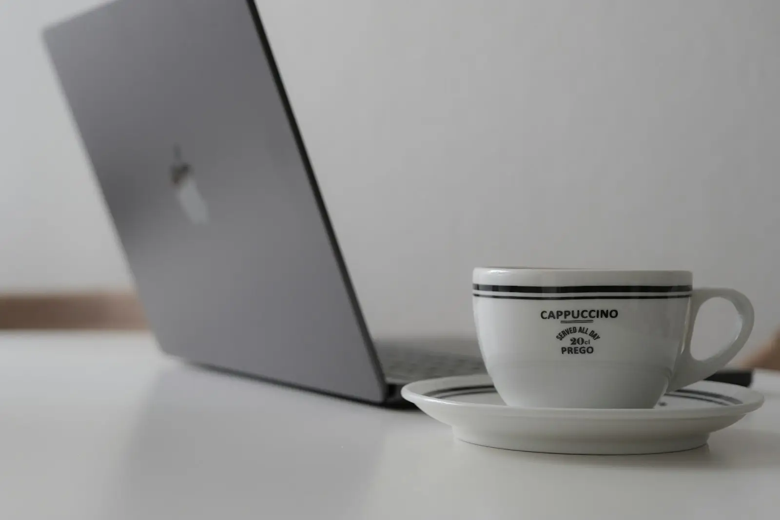 Un portátil y una taza de café sobre un escritorio blanco