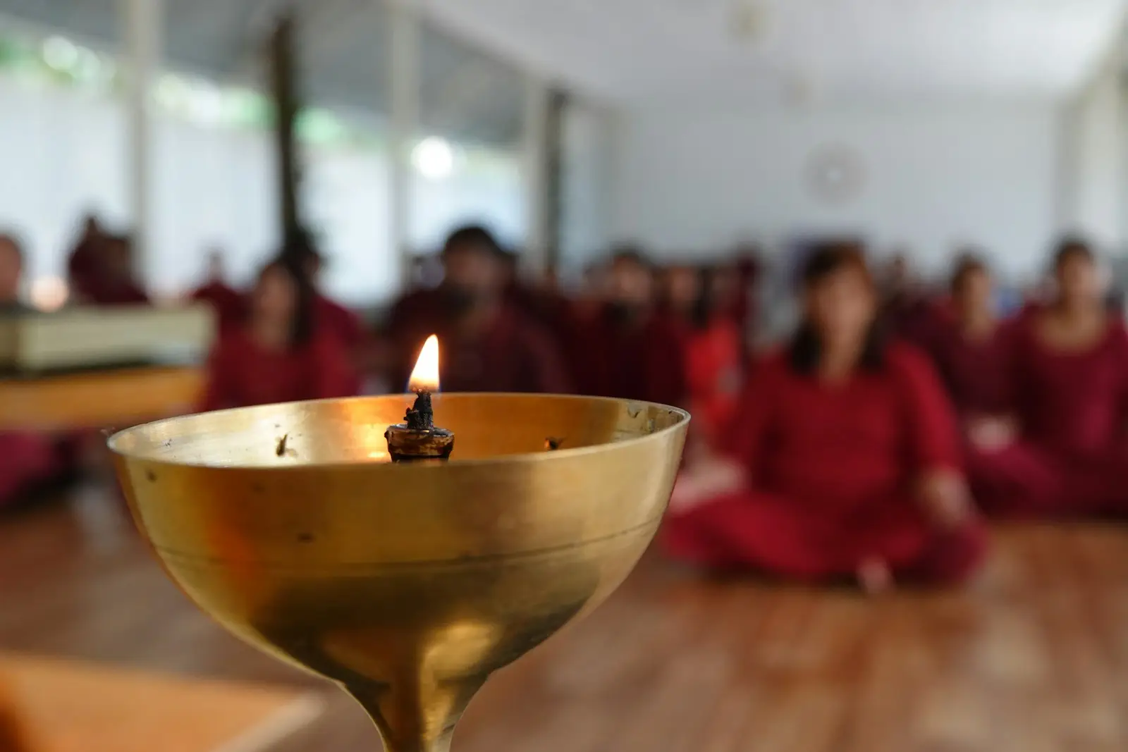 Una vela encendida en un cuenco dorado con un grupo meditando al fondo